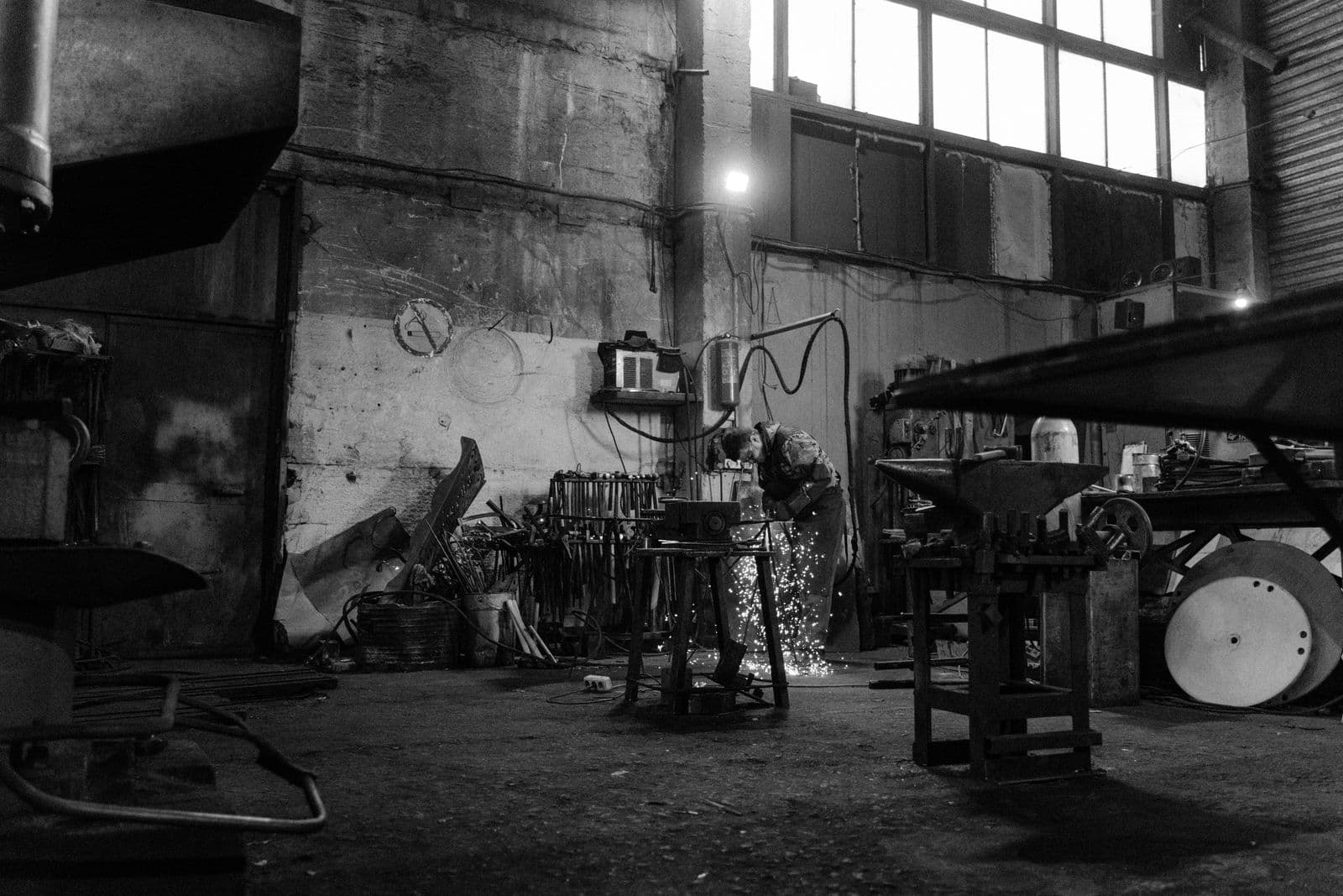 A blacksmith uses a grinder in a workshop producing sparks. Industrial setting.
